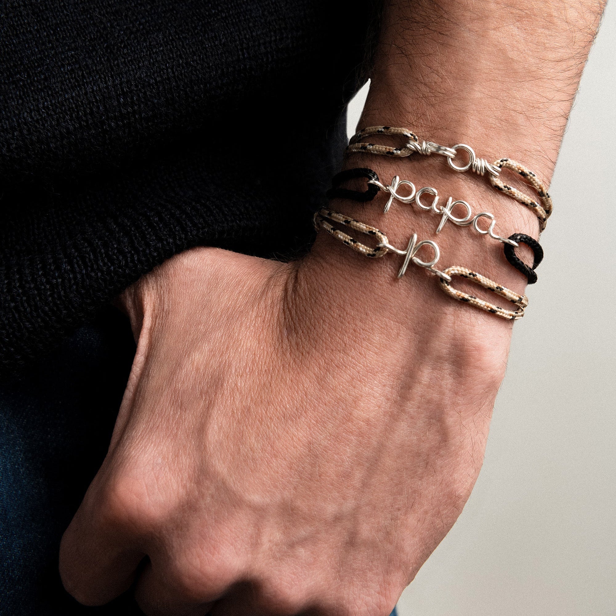 A close-up of man silver bracelets stack, including a 'papa' personalised bracelet from Atelier Paulin Australia