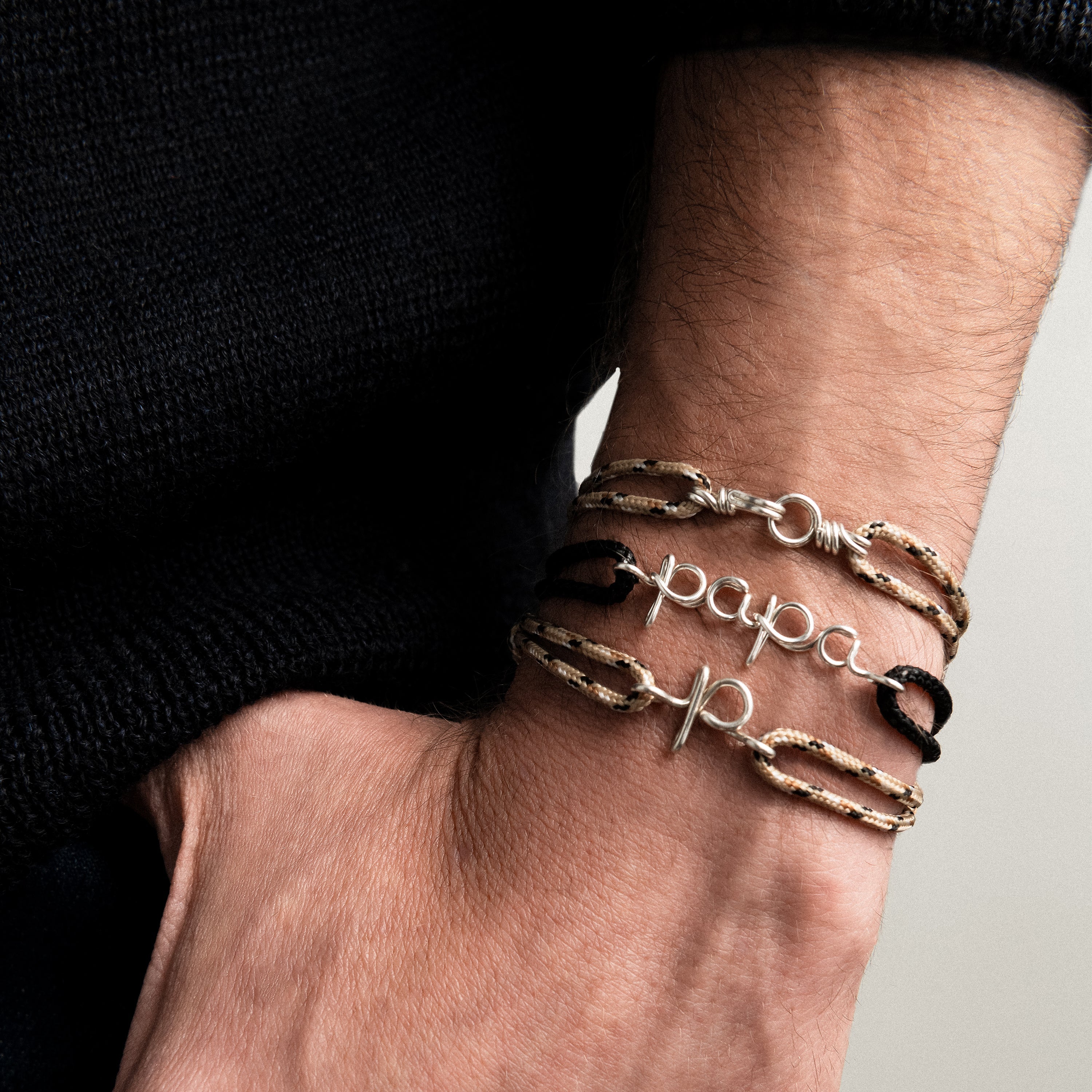 Close-up of a wrist wearing multiple bracelets with 'papa' and 'p' on a neutral background