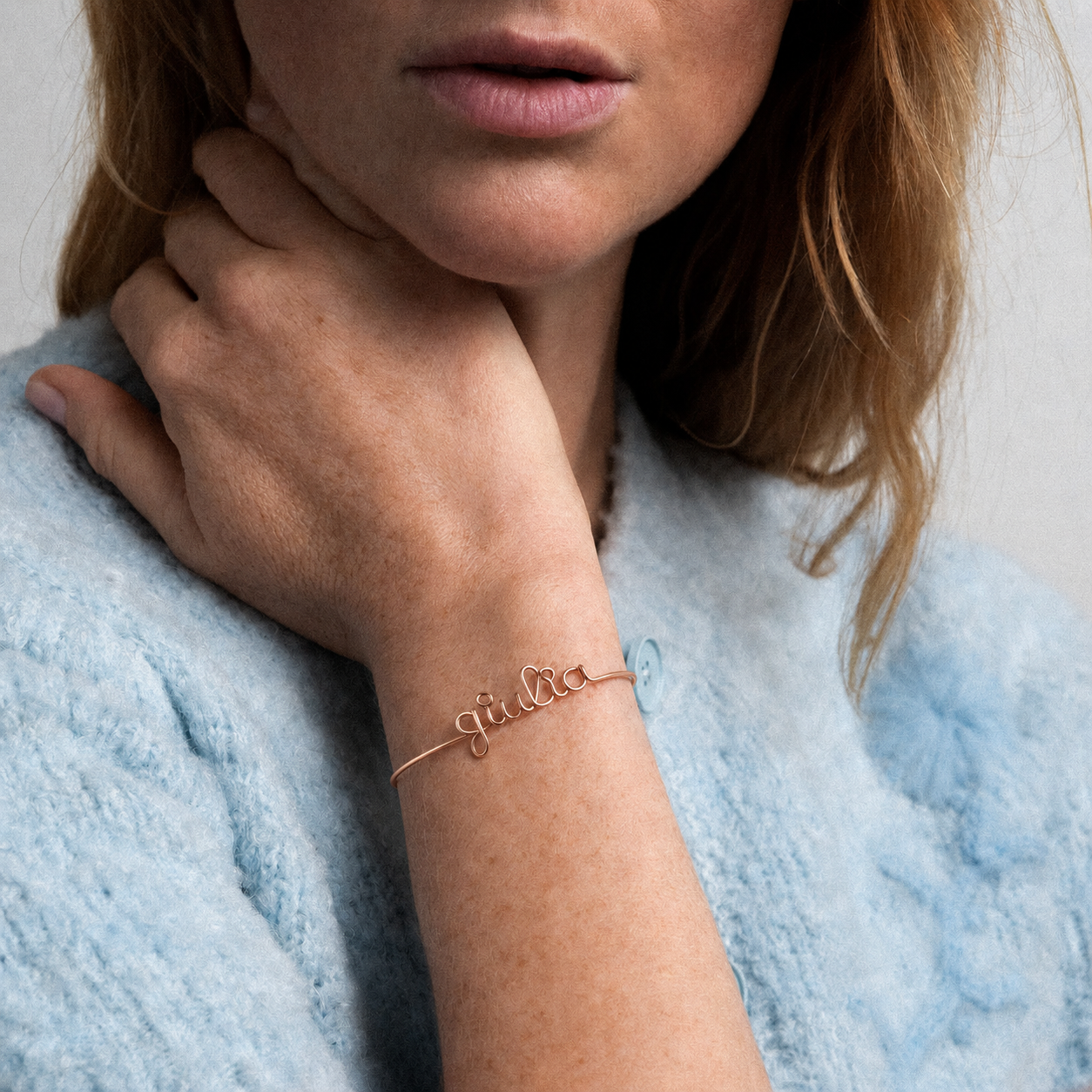Person wearing a rose gold bracelet with personalised name on it, against a light blue jumper.
