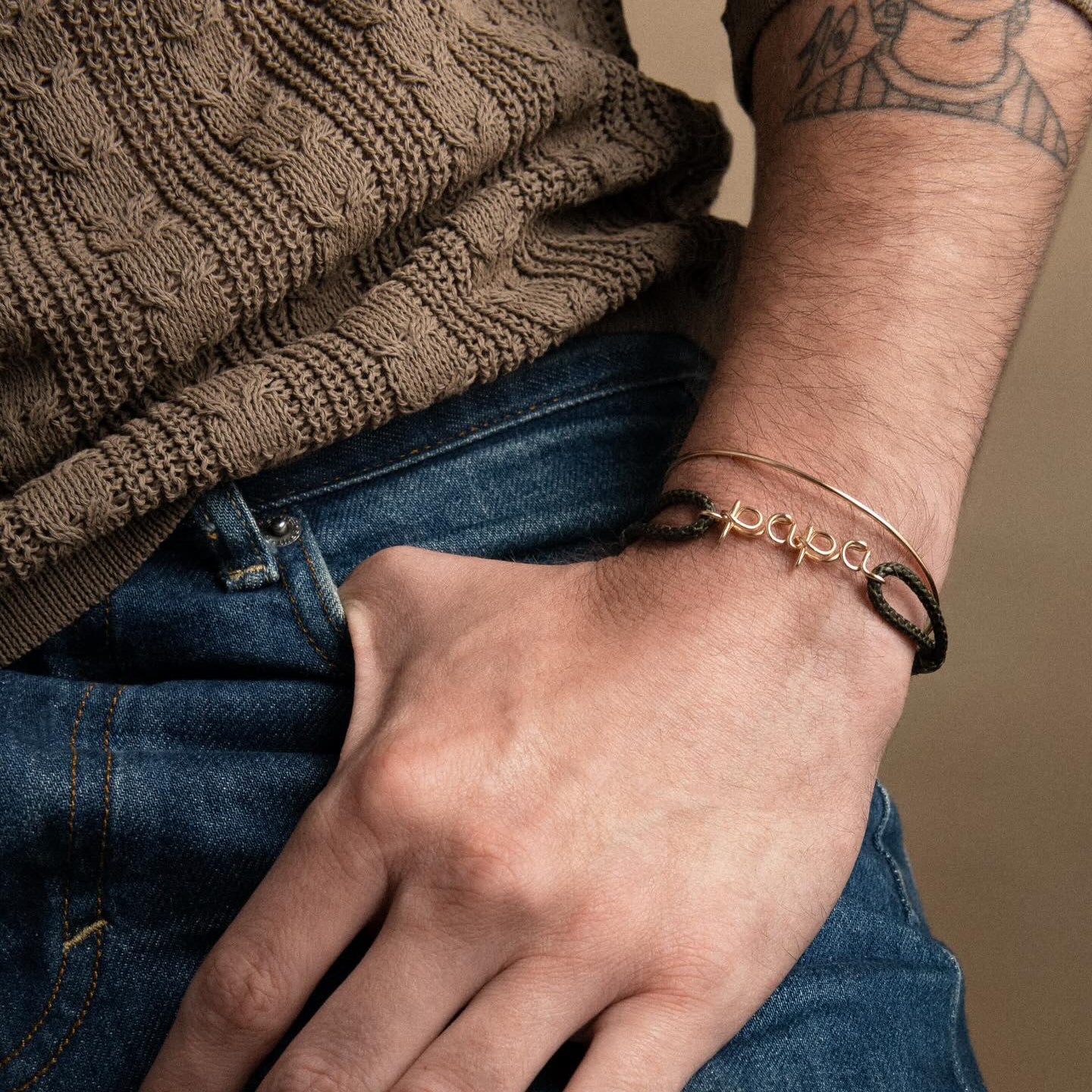 Man wearing Atelier Paulin cord bracelet with gold letters cursive writing 'Papa' - handcrafted in Paris.